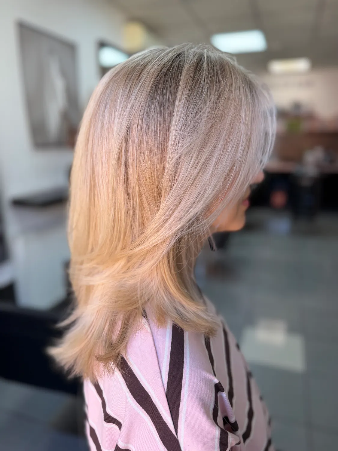 Vrstvený strih v blond odtieni, v pozadí interiér salónu MHair